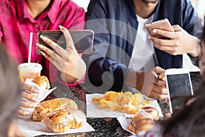 Group of unrecognizable people busy on mobile while having snacks together at restaurant - Concept of millennials having junk food