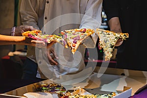 Group of unrecognizable peoples hands holding a slice of pizza.