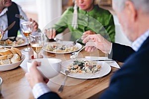 Group of unrecognizable senior friends at dinner party at home, eating.