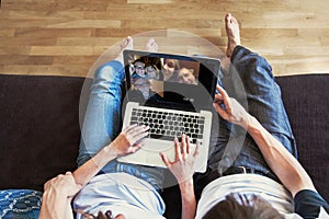 group video call with family and friends, couple sitting on the couch using laptop