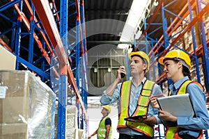Group of warehouse workers with hardhats and reflective jackets using tablet, walkie talkie radio and cardboard while controlling