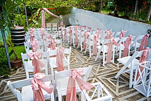 Group of white banquet chairs, decorated with pink sashes for a wedding ceremony photo