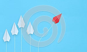 Group of white paper planes in one direction and one red paper plane pointing in different way on blue background. Business for