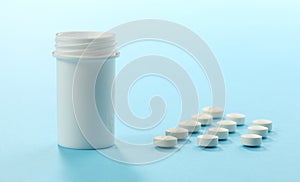 Group of white pills and plastic bottle on blue