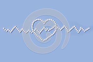 Group of white round pills forms heart figure next to heart rhythms from white pills on a blue background.