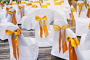 A group of white spandex chairs cover with gold organza sash for beach wedding venue arrangement