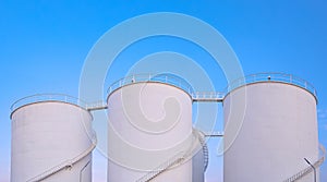 Group of white storage fuel tanks in oil industrial area against blue sky background