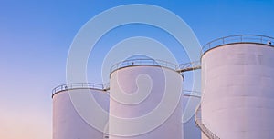 Group of white storage fuel tanks in petrochemical industrial area against dusk sky background in evening time