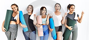 Group of women holding yoga mat standing over isolated background with a big smile on face, pointing with hand finger to the side