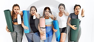 Group of women holding yoga mat standing over isolated background pointing displeased and frustrated to the camera, angry and