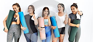 Group of women holding yoga mat standing over isolated background pointing fingers to camera with happy and funny face