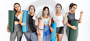 Group of women holding yoga mat standing over isolated background pointing with hand finger to the side showing advertisement,