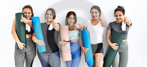 Group of women holding yoga mat standing over isolated background pointing to you and the camera with fingers, smiling positive