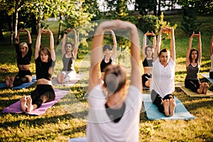 Group of women are practicing yoga and sits with hands up morning in city park