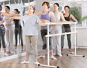 Group of women stand in second position at barre