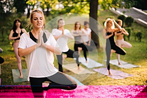 Group of women are standing on yoga mats and balancing on leg in pose tree