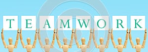 Group of wooden figure standing and holding text label in words Teamwork.