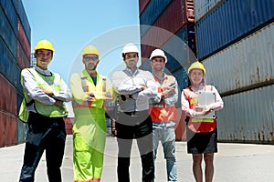 Group of worker team with helmet and safety vest stand in line with arms crossed at logistic shipping container yard. Woman and