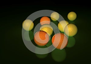 Group of yellow and orange golf balls, glowing on a reflecting surface