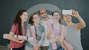 Group of yoga students taking selfie in studio using smartphone camera smiling