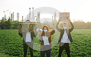 Group of young activists with placards standing outdoors by oil refinery, protesting.