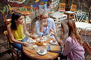 Group of young adult caucasian female friends talking and laughing in outdoor cafe, drinking coffee