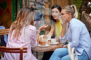 Group of young adult caucasian female friends talking, sitting in outdoor cafe, drinking coffee