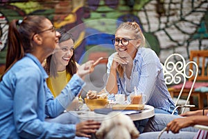Group of young adult female friends talking and laughing in outdoor cafe, drinking coffee