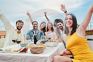 Group of young adult friends having fun and laughing on a dinner party rooftop. Happy multiracial people celebrating a