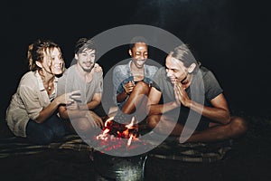 Group of young adult friends sitting around the bonfire outdoors recreational leisure and friendship concept