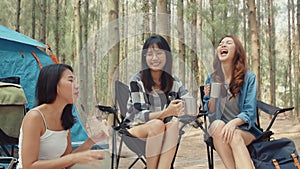 Group of young asia camper friends sitting in chairs by tent in forest. Teenager girl traveler relax and talk on a summer day at