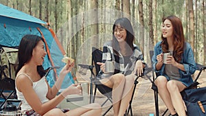Group of young asia camper friends sitting in chairs by tent in forest. Teenager girl traveler relax and talk on a summer day at