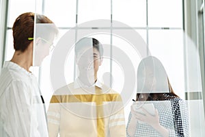 Group of young asian attractive business people standing, talking and listening to meeting with manager behind transparent glass w