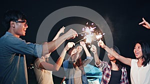 Group of young Asian college student friends lit light sparkler, sing and dance together at beach camping tent