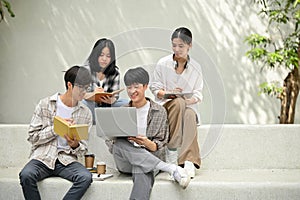 Group of young Asian college students sitting on a bench in a campus relaxation area