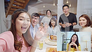 Group of young Asian people look at camera, remote video call greeting with friend at home dinner party