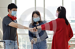 Group of young Asian travelers wearing face mask standing in the airport terminal greeting with a fist bump for a new normal