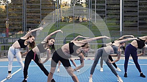 Group of young attractive women doing tiltes left to right on the fitness lesson on the sportground in the park