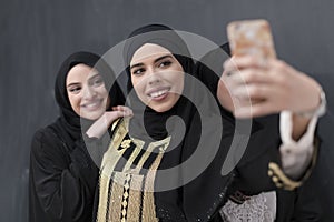 Group of young beautiful muslim women in fashionable dress with hijab using smartphone while taking selfie picture in