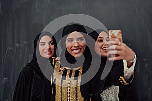 Group of young beautiful muslim women in fashionable dress with hijab using smartphone while taking selfie picture in