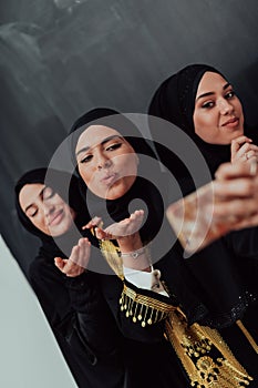 Group of young beautiful muslim women in fashionable dress with hijab using smartphone while taking selfie picture in