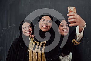 Group of young beautiful muslim women in fashionable dress with hijab using smartphone while taking selfie picture in