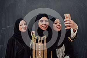 Group of young beautiful muslim women in fashionable dress with hijab using smartphone while taking selfie picture in