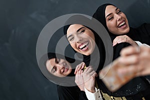 Group of young beautiful muslim women in fashionable dress with hijab using smartphone while taking selfie picture in