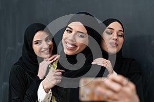 Group of young beautiful muslim women in fashionable dress with hijab using smartphone while taking selfie picture in