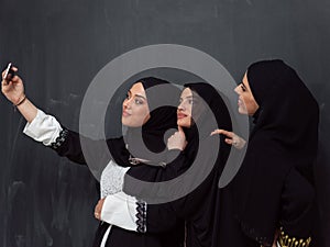 Group of young beautiful muslim women in fashionable dress with hijab using smartphone while taking selfie picture in