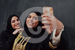 Group of young beautiful muslim women in fashionable dress with hijab using smartphone while taking selfie picture in