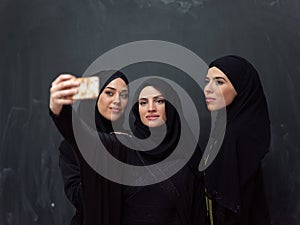 Group of young beautiful muslim women in fashionable dress with hijab using smartphone while taking selfie picture in