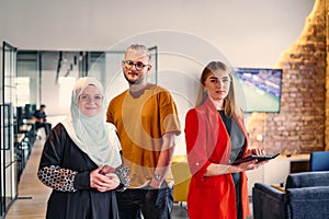 A group of young business colleagues, including a woman in a hijab, stands united in the modern corridor of a spacious