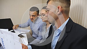 Group of young business people sitting at table in modern office and working on new project. Colleagues carefully look